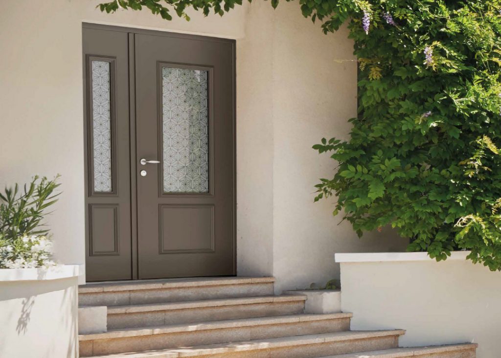 Porte d'entrée double vantaux vitrée taupe avec motifs géométriques, entourée de verdure et escalier en pierre