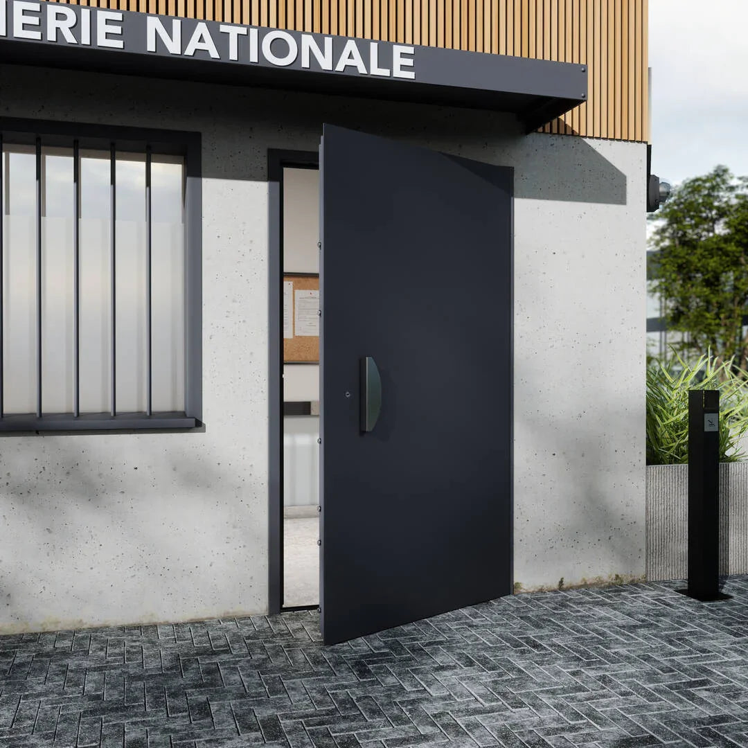 Porte d'entrée métallique noire ouverte sur bâtiment public avec murs en béton et sol pavé