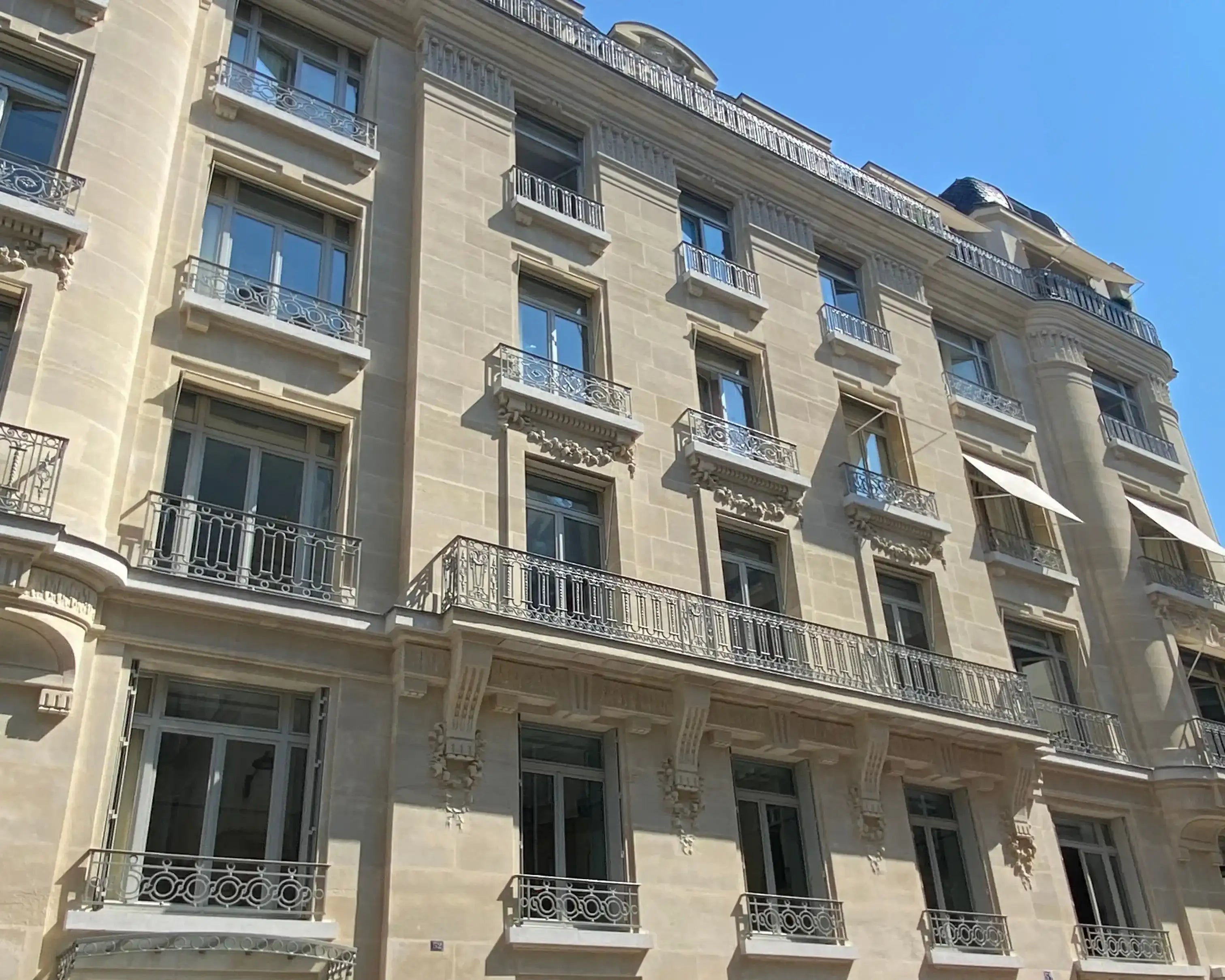 Façade haussmannienne rénovée à Paris avec balcon en fer forgé sous ciel bleu, entreprise de rénovation Renobat