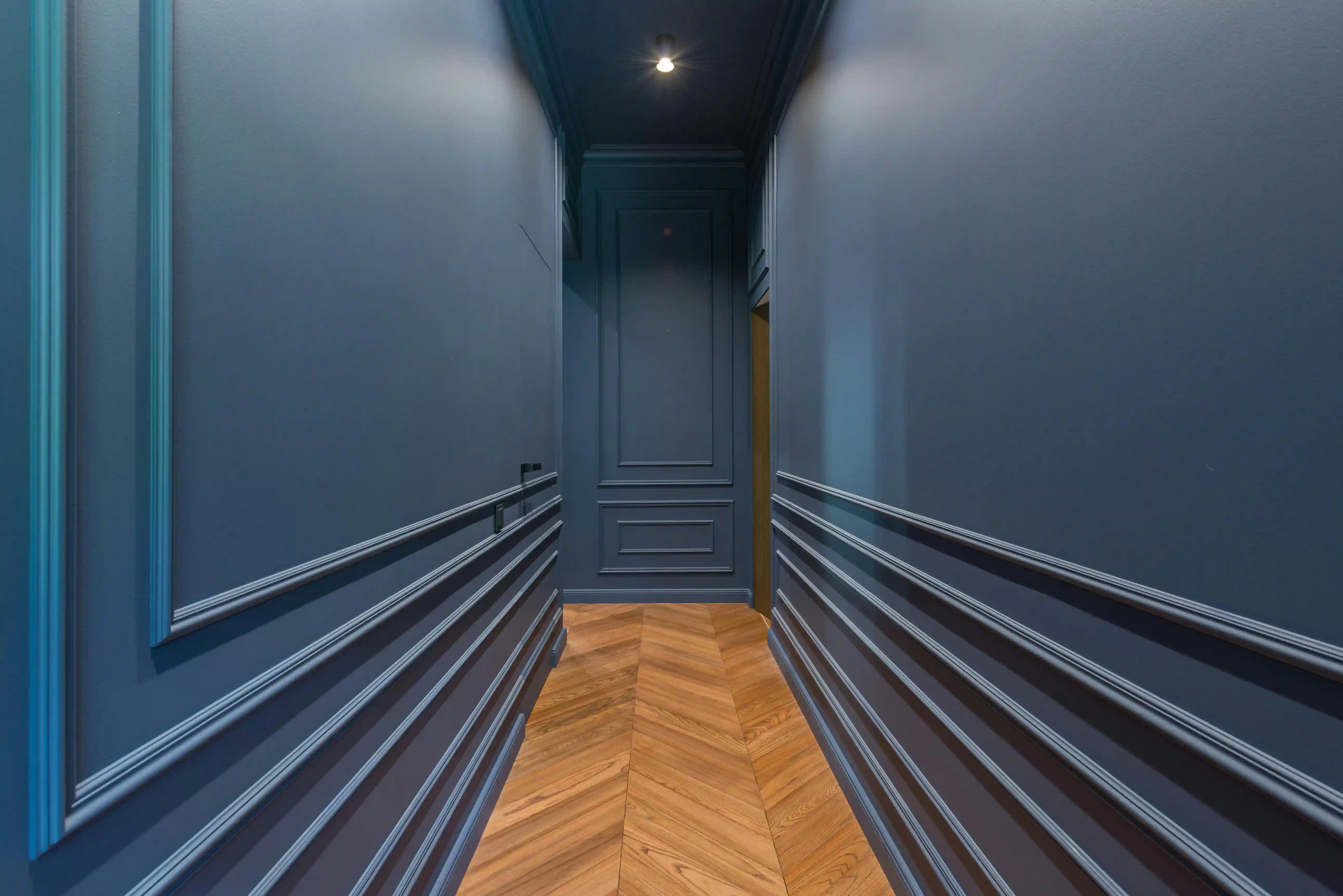 Parquet massif chêne en pose chevron (point de Hongrie) dans un couloir aux boiseries classiques. Cette technique de pose traditionnelle apporte sophistication et élégance, créant un jeu de lumière unique qui sublime les espaces de circulation.