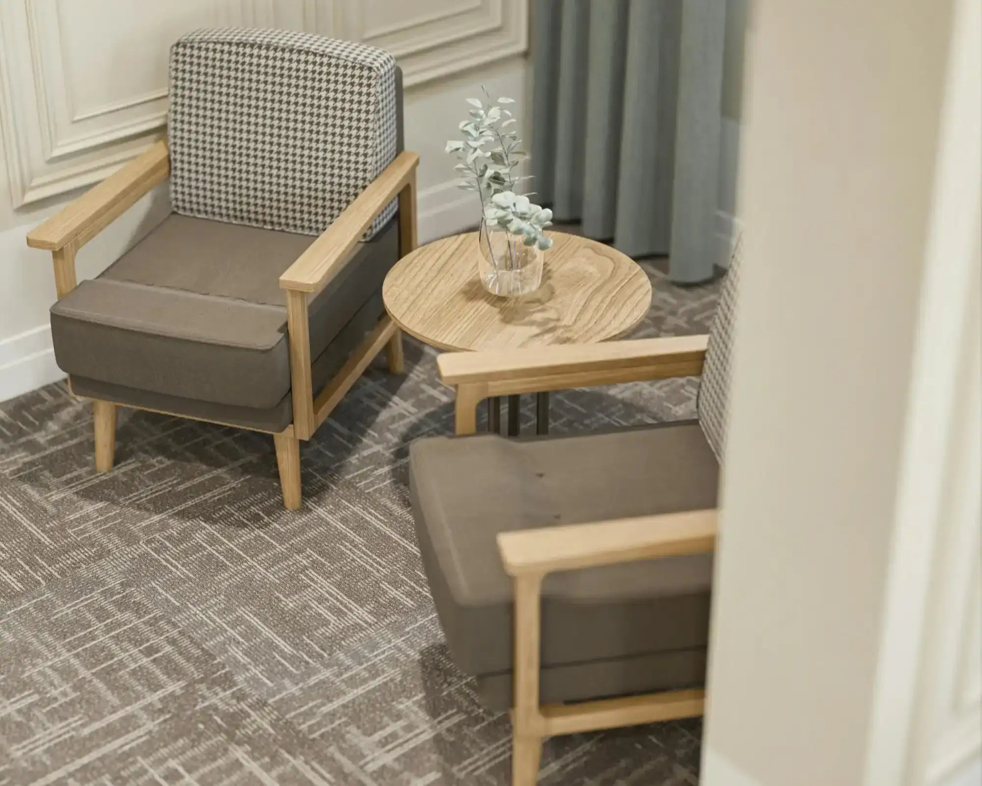 Coin salon intérieur avec deux fauteuils en bois et tissu gris, petite table ronde en bois avec vase et décoration