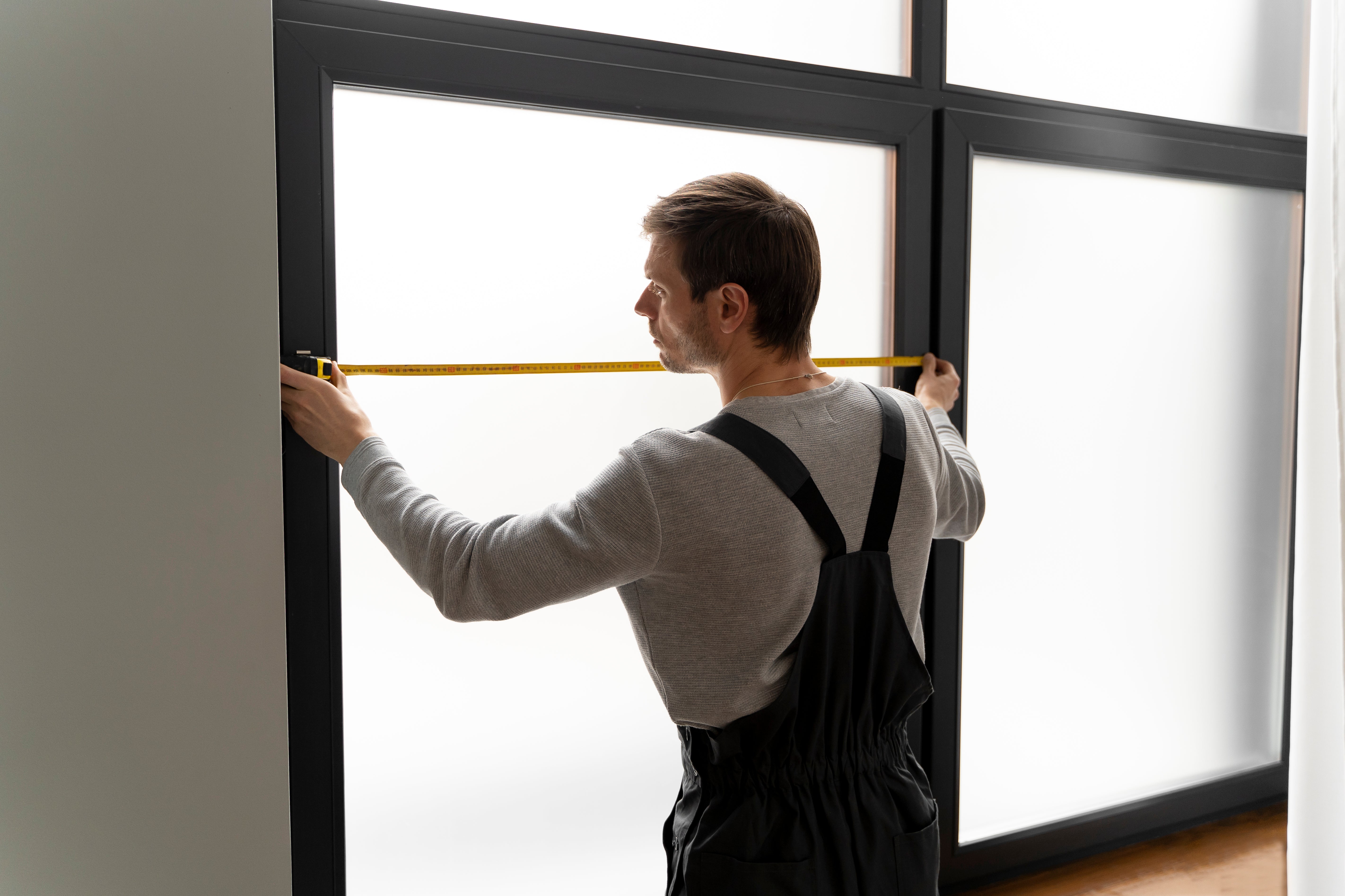 Menuisier professionnel mesurant une fenêtre avec un mètre pour une installation sur mesure à Courbevoie